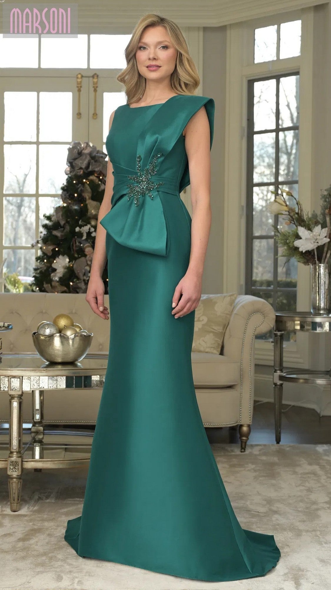 A woman stands elegantly in the Marsoni MV1359 long formal dress, its emerald stretch Mikado fabric and mermaid skirt highlighting her graceful silhouette.